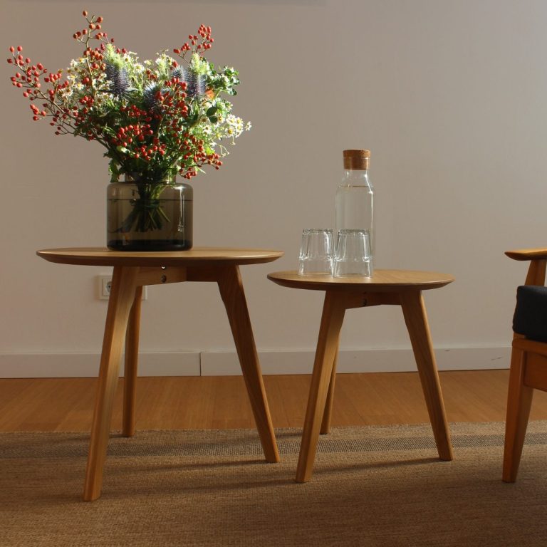 Freundlicher, heller Therapieraum Zwei Holztische mit einer Blumenvase und Wassergläser, sowie ein im Bildrand erkennbarer Stuhl