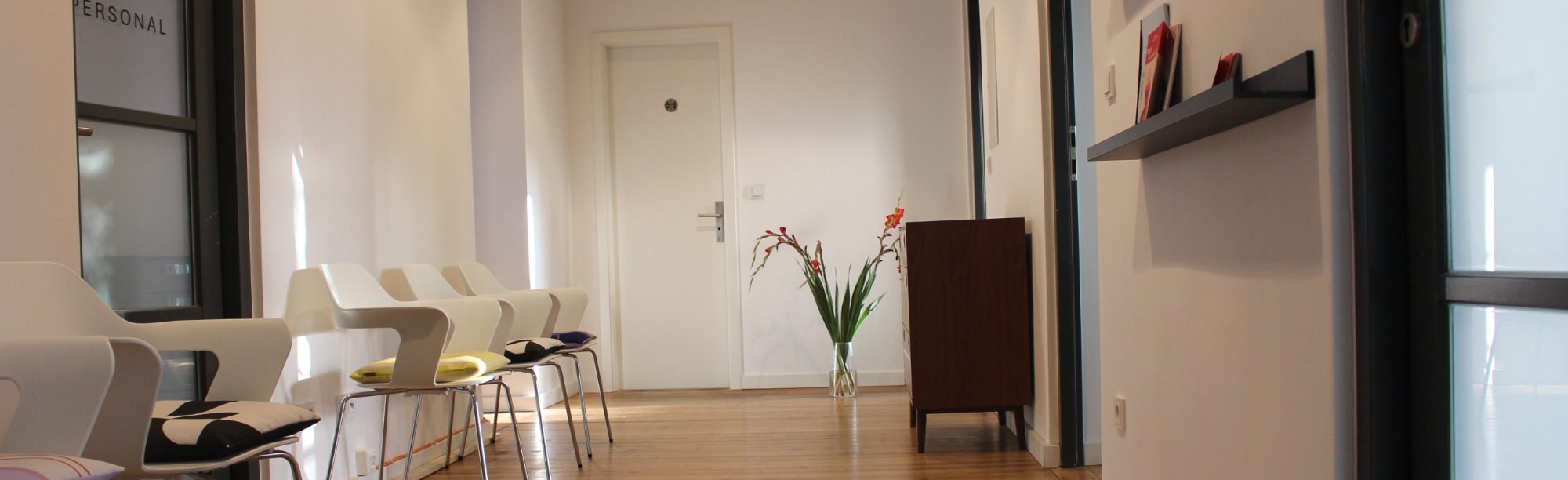 Moderner, heller Empfangs- und Wartebereich von psyvia, mit weißen Designer-Stühlen, Holzboden und Deko-Pflanze