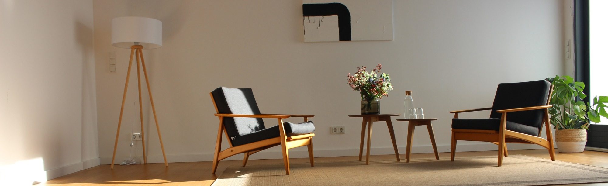 Freundlicher, moderner Therapieraum mit zwei Stühlen, Tisch und Blumenstrauß in einem lichtdurchfluteten Raum