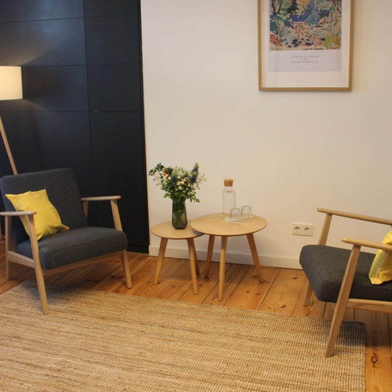 Therapie-Sitzecke unserer Praxis Gemütliche Sitzecke mit zwei Stühlen, Tisch und einer Vase mit Blumen